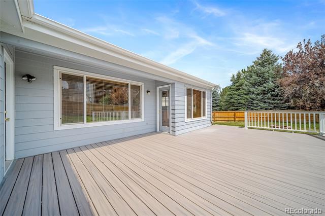 Spacious gray deck beside a light blue home, with white railing and mature trees beyond.