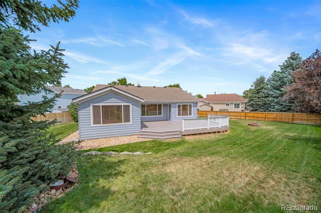 Gray-sided home with a raised deck and white railing overlooking a fenced lawn.