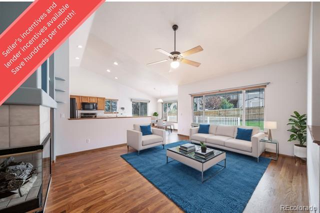 Staged living room with a blue rug, light sofas, hardwood floors, and a fireplace.