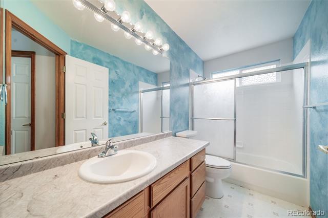 Bathroom with a marble-look vanity, wood cabinets, and a glass-enclosed tub-shower.