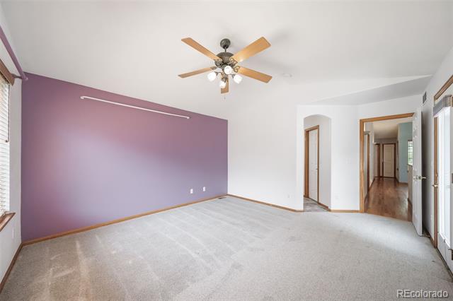 Vacant bedroom with a purple accent wall, light carpet, and a wood-blade ceiling fan.