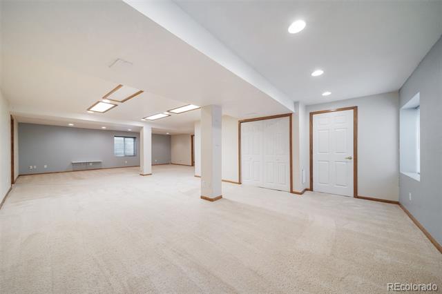 Empty carpeted room with recessed lights, white paneled doors, and an adjoining open area.
