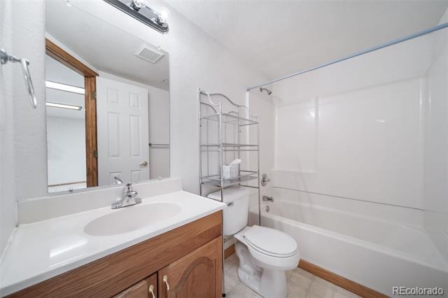 Bathroom with a white tub and shower, toilet, and wood-front vanity.
