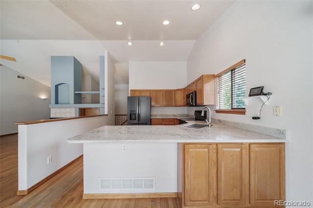 Kitchen with a stone-countertop peninsula, honey-colored cabinets, dark refrigerator, and hardwood floors.