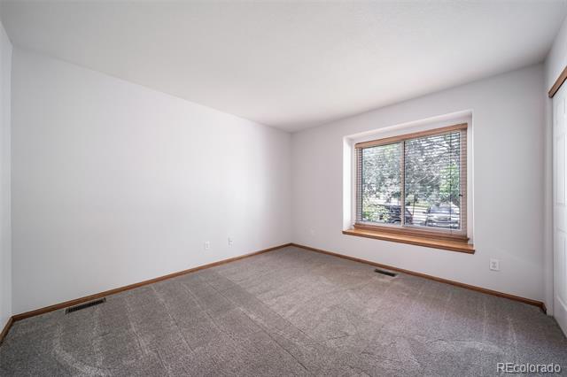 Vacant bedroom with gray carpet and a wide window with blinds.