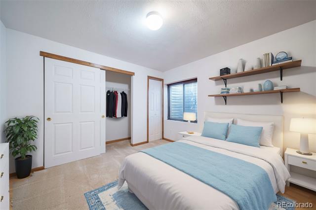 Staged bedroom with pale blue bedding, open closet, and floating shelves.