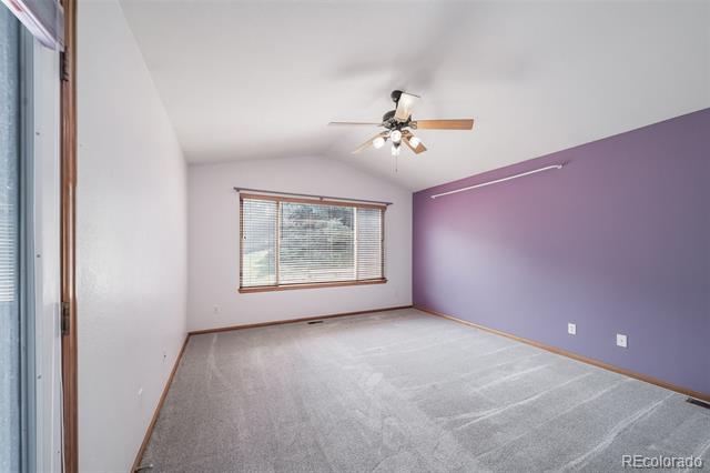 Empty bedroom with gray carpet, purple accent wall, window with blinds, and ceiling fan.