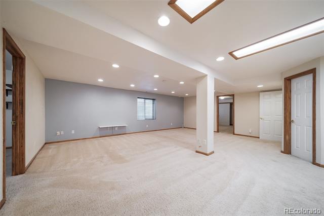 Open carpeted room with gray walls, recessed lighting, a small window, and several doorways.