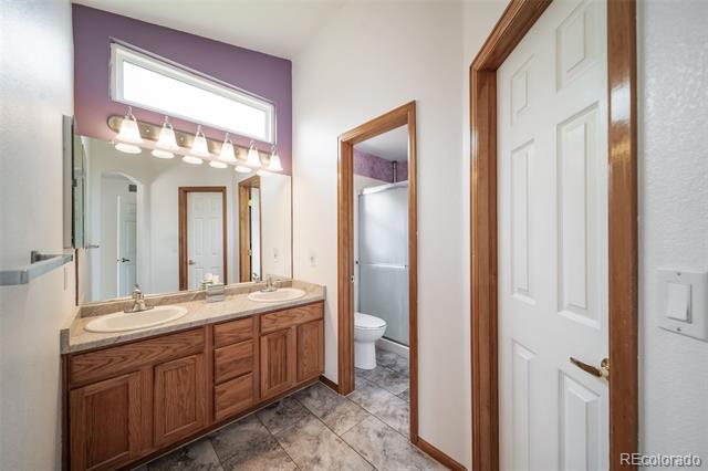 Bathroom with a double-sink wood vanity and an open doorway to a toilet and shower.