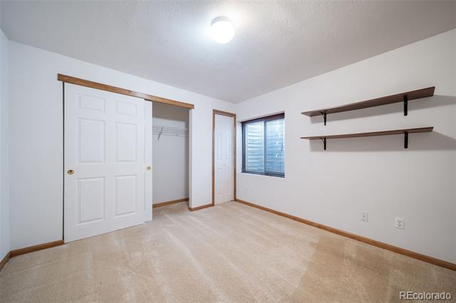 Empty bedroom with a sliding-door closet, wall-mounted shelves, and a window with blinds.
