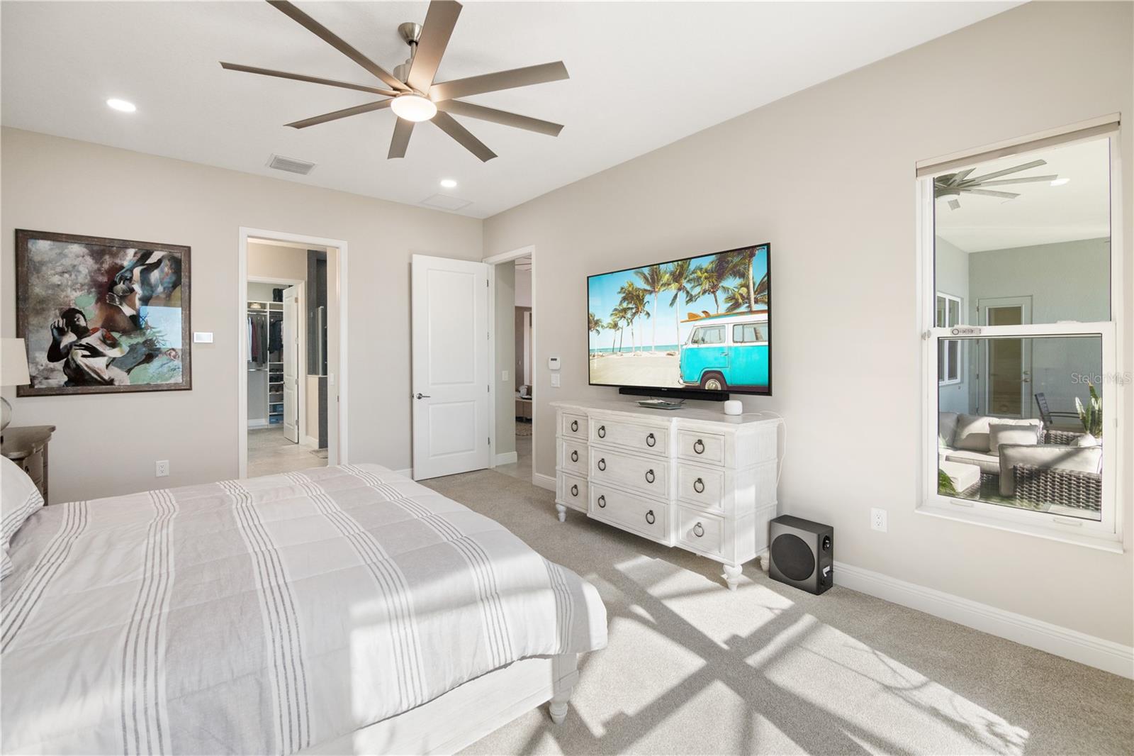 Bedroom with striped white bedding, a large ceiling fan, and a television above a white dresser.