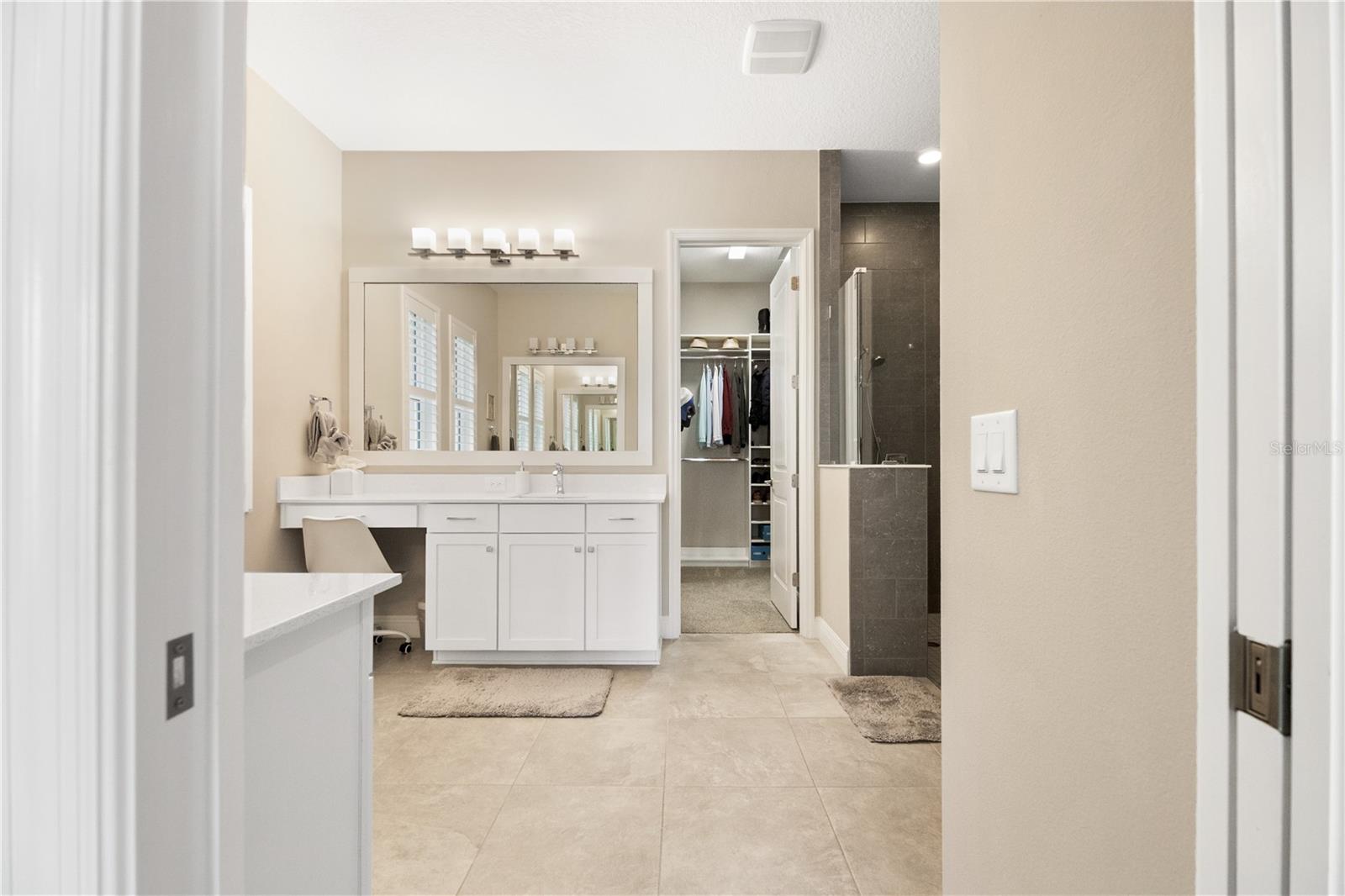 Primary bathroom with a long white vanity, tiled glass shower, and open walk-in closet.