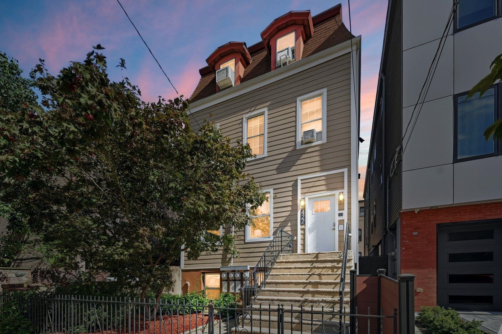 Gray-sided home with broad front steps and warmly lit windows beneath a pink dusk sky.