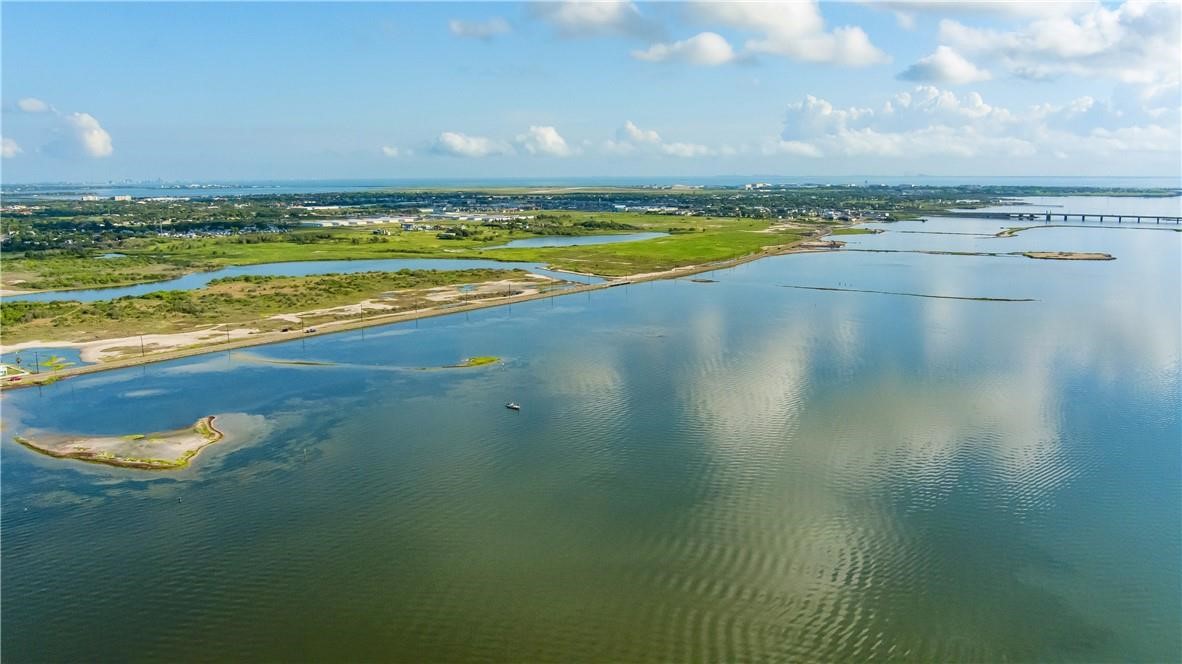 Aerial coastal lagoon with marshy shoreline and a distant bridge.