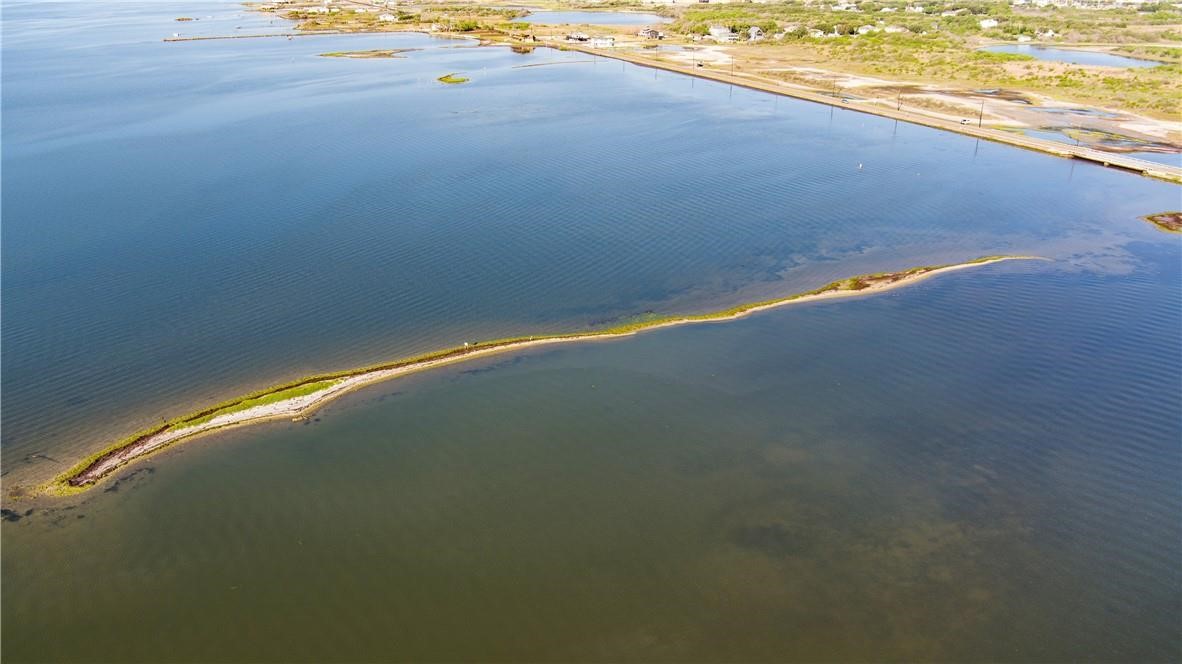 Aerial view of coastal water, with a narrow vegetated sandbar and distant shoreline road.