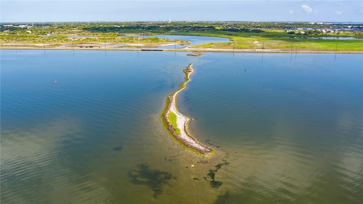 Aerial view of a curved sandbar extending into coastal water, with shoreline in the distance.