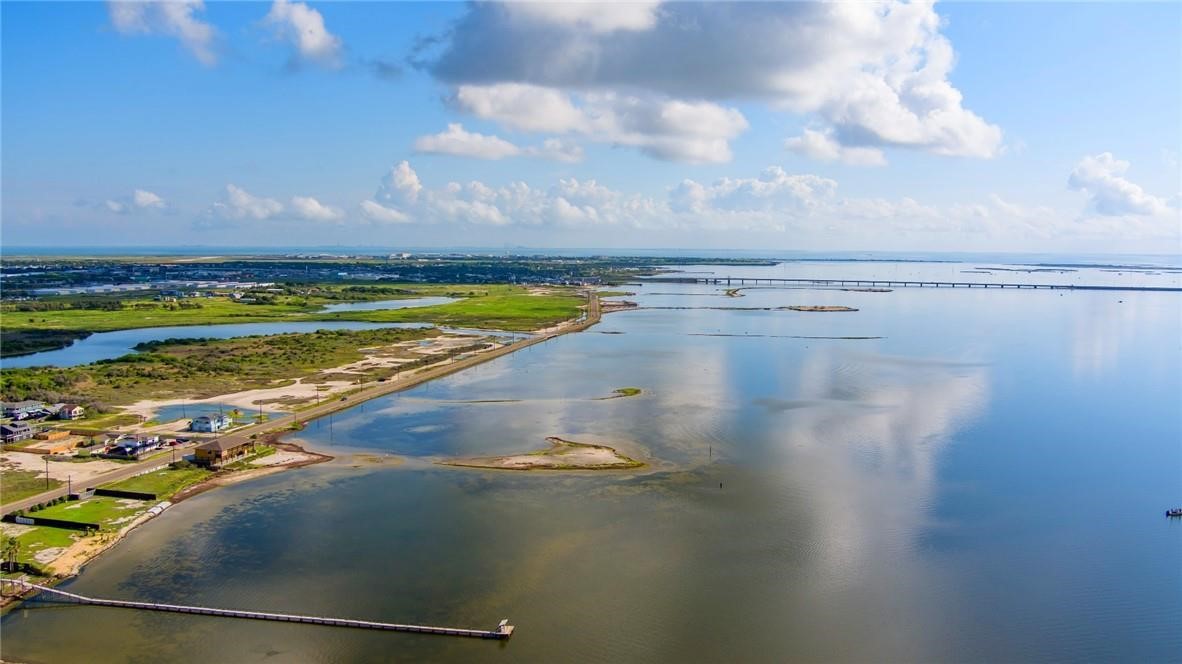 Aerial view of a coastal bay, with marshland, shoreline homes, and a long bridge in the distance.