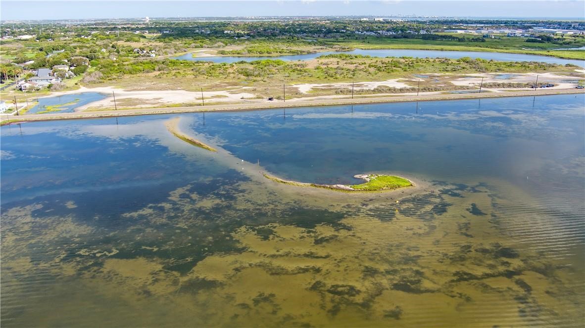 Aerial view of coastal water, with a green sandbar and marshy shoreline beside a narrow road.