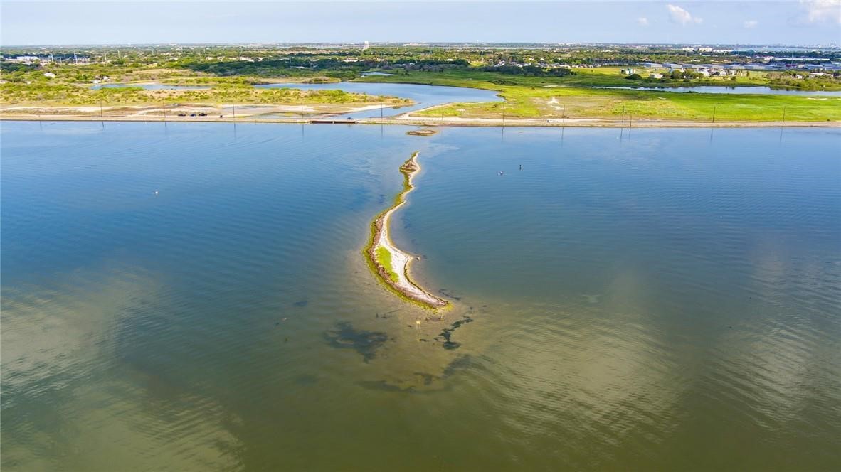 Aerial view of a narrow curving strip of land extending into a lagoon, with marshland beyond.