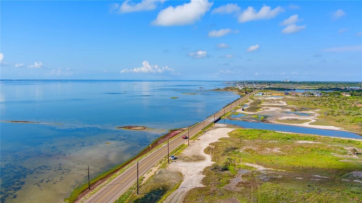 Aerial view of a coastal road tracing the shoreline beside blue water and marshland.