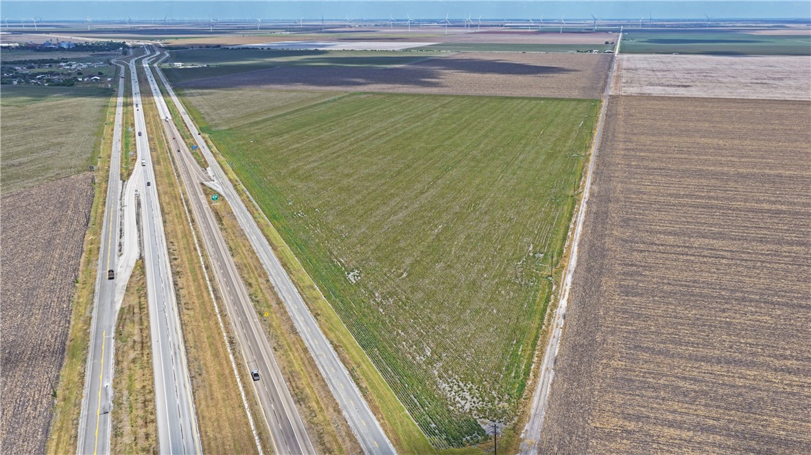 Cultivated land beside a divided highway, with surrounding fields and distant wind turbines.