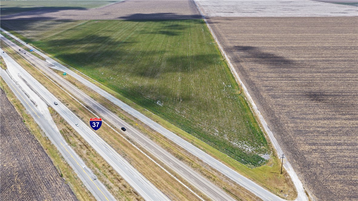 Aerial view of green agricultural land beside Interstate 37, bordered by cultivated fields.