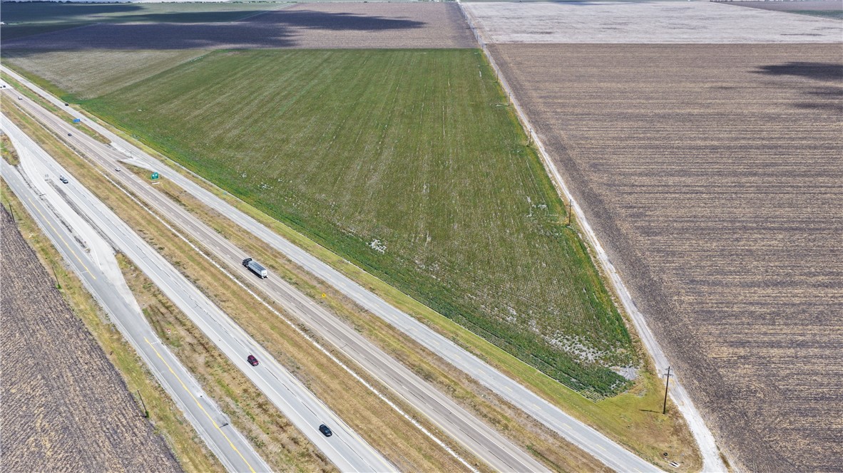 Aerial view of a green field beside a divided highway, bordered by brown tilled farmland.
