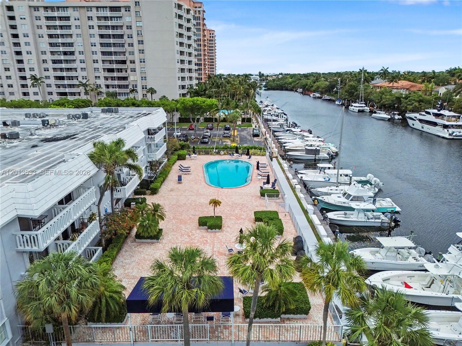 Waterfront condominium pool and palm-lined terrace beside a marina and canal.
