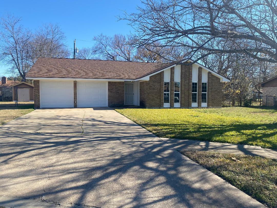 Brick ranch house with two white garage doors, tall front windows, and a wide concrete driveway.