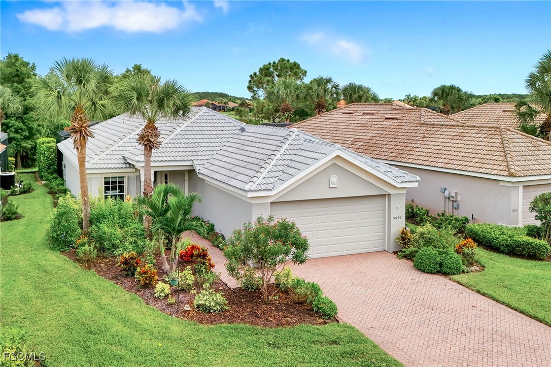 Single-story home with a gray tile roof, two-car garage, brick driveway, and palm-landscaped yard.
