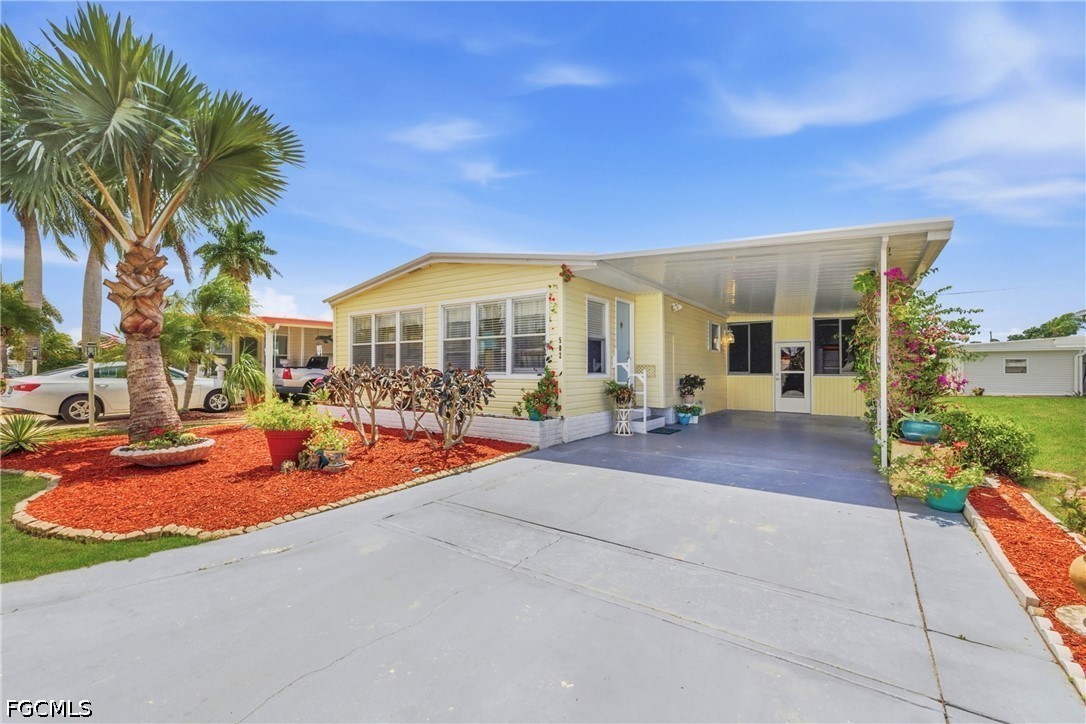 Yellow single-story home with a covered carport, palm trees, and red-mulch landscaping.