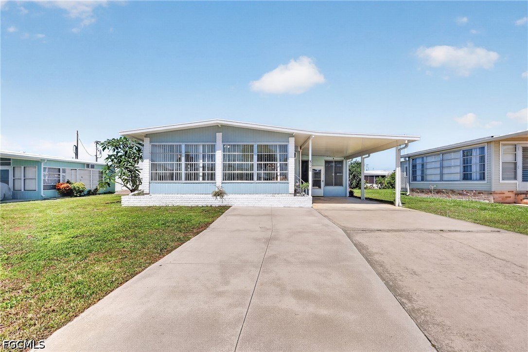 Light-blue single-story home with an enclosed porch, covered carport, and wide concrete driveway.