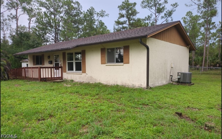 Single-story cream house with a small wooden porch, brown shutters, and pine trees behind it.