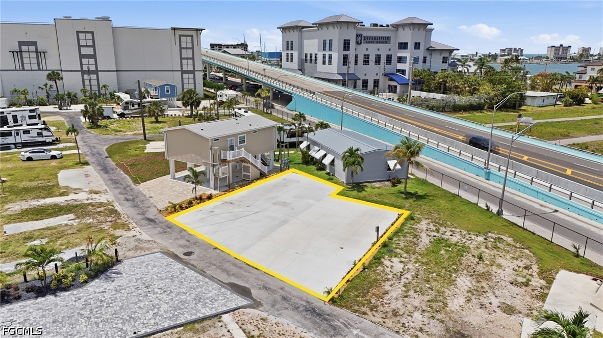 Vacant paved lot outlined in yellow beside an elevated roadway, with water visible in the distance.