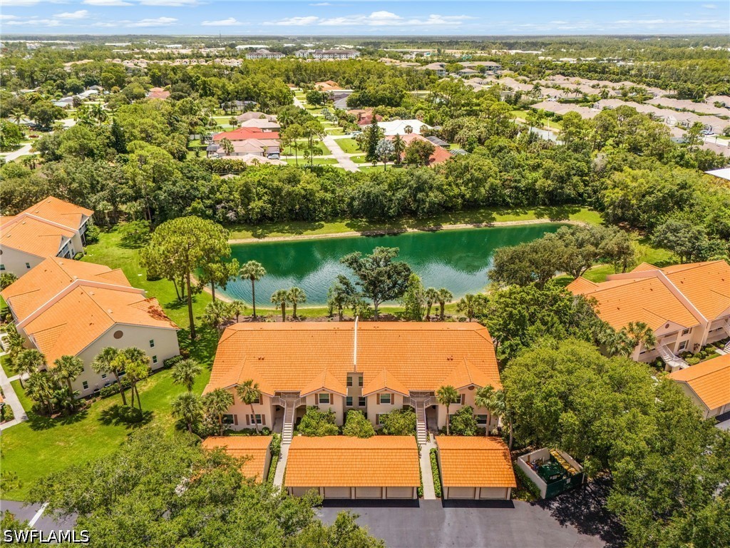 Aerial view of a residential community surrounding a tree-lined lake, with orange tile roofs.