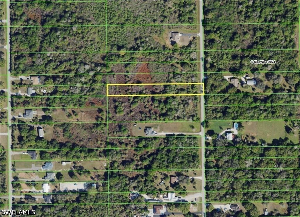 Wooded parcel outlined in yellow among homes and roads.