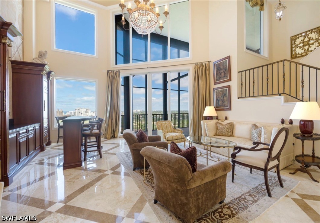 Two-story living room with a crystal chandelier, marble floors, and tall windows overlooking distant buildings.