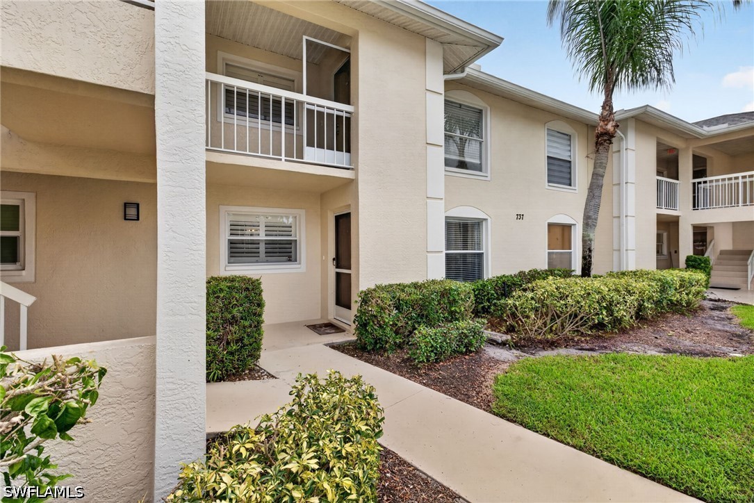 Two-story beige condominium exterior with balconies, trimmed hedges, and a walkway to unit 737.