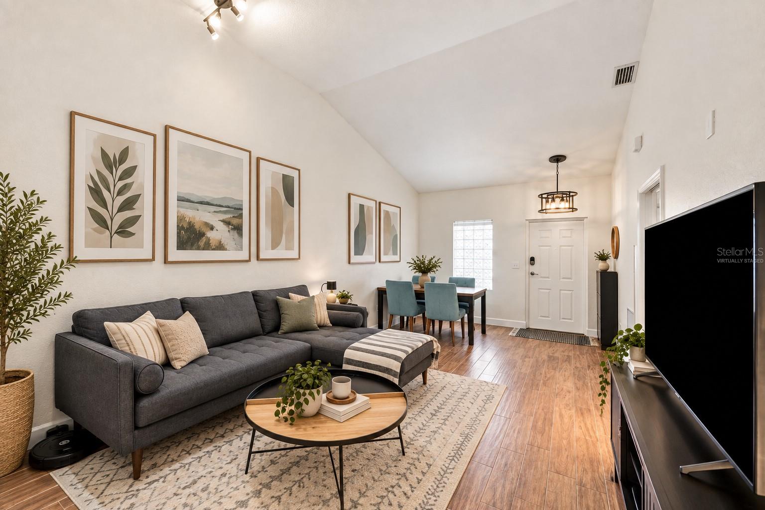 Living room with a gray sectional, vaulted ceiling, and dining nook with teal chairs.