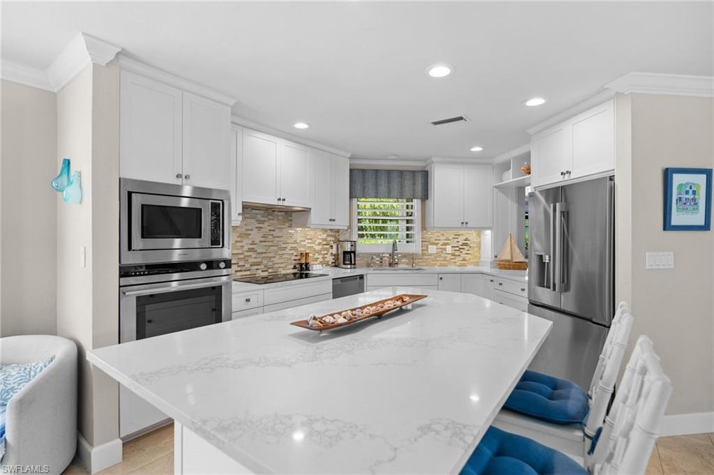 Bright kitchen with white cabinetry, a stone island, stainless appliances, and a mosaic tile backsplash.