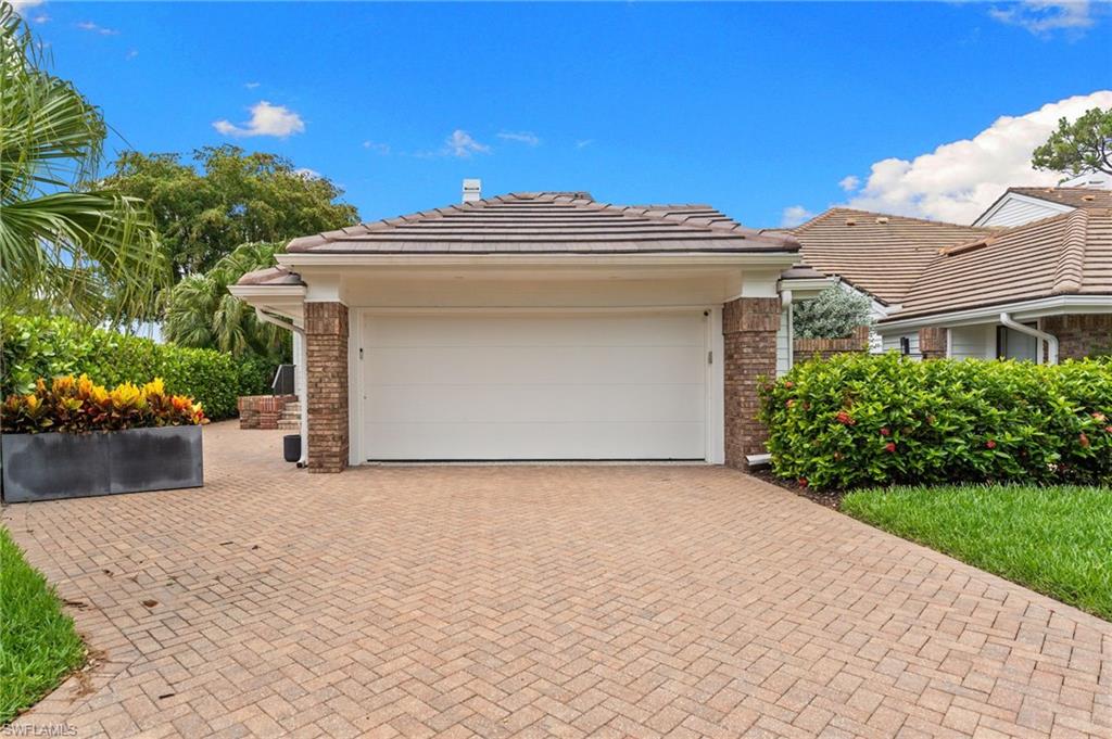 Home exterior with a wide garage, brick-paver driveway, and tropical landscaping.
