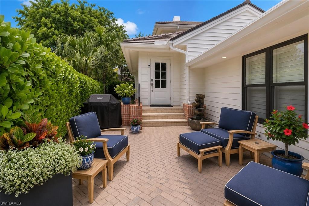 White home’s courtyard patio with navy-cushioned chairs, potted flowers, and a small fountain.