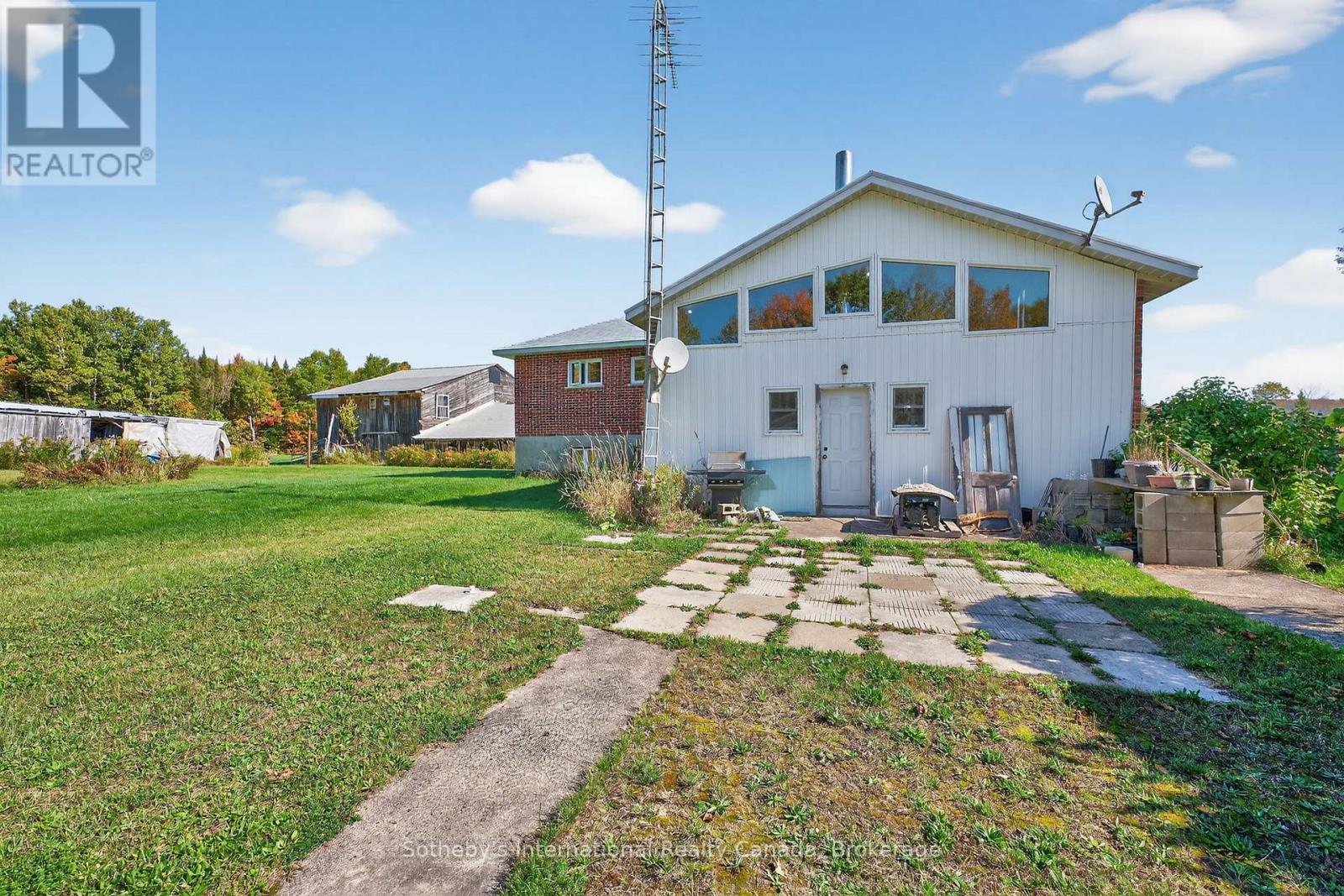 White-sided and red-brick house with a broad lawn, concrete walkway, and tall antenna.