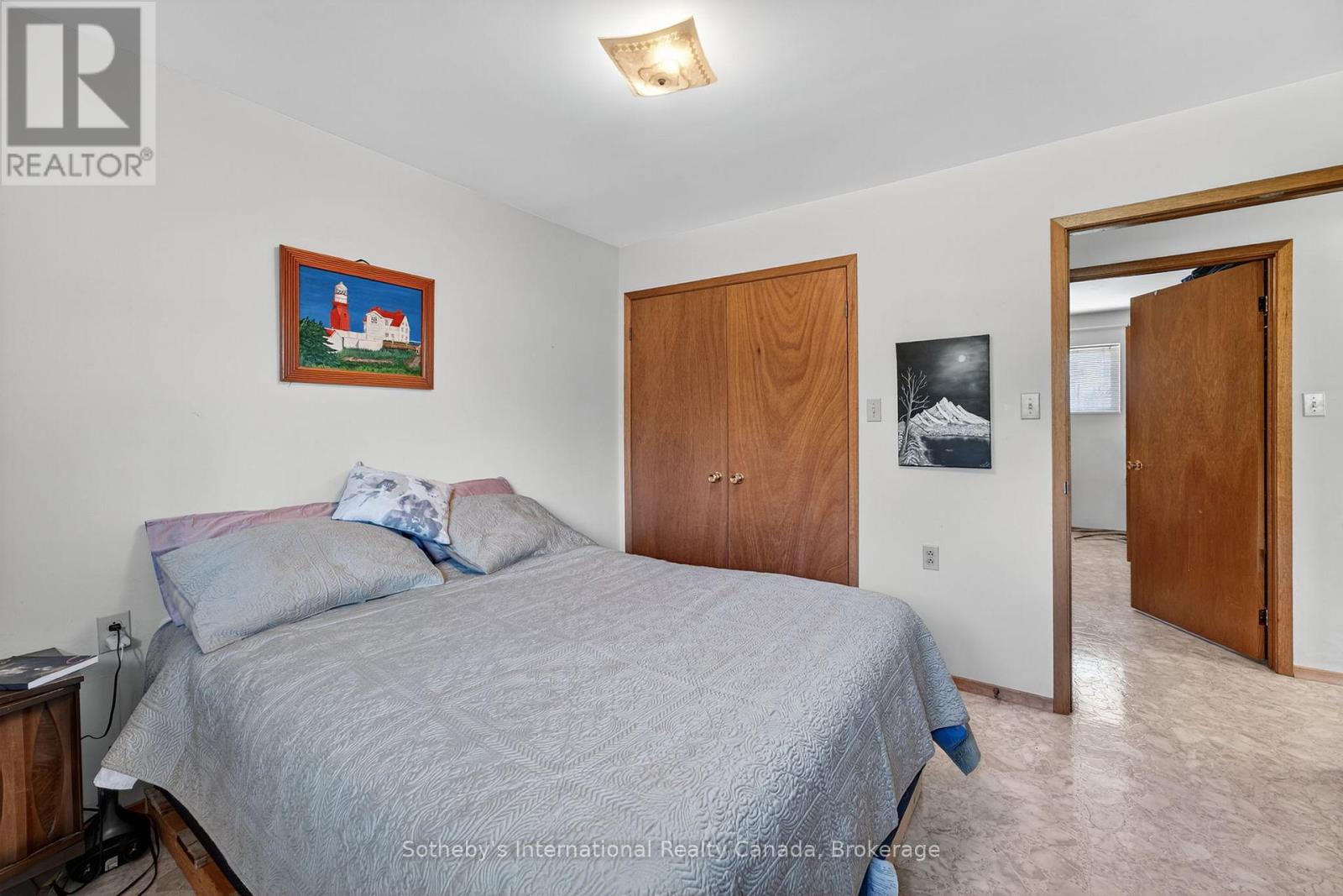 Bedroom with a large gray-quilted bed, wood closet doors, and an open doorway.