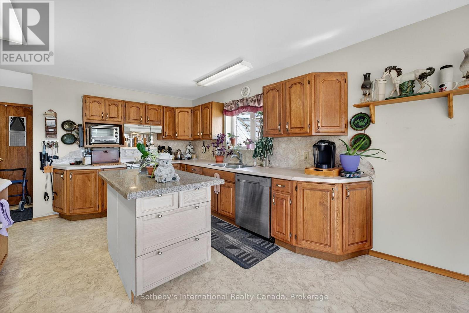 Kitchen with warm wood cabinets, a white island, stone counters, and stainless-steel dishwasher.