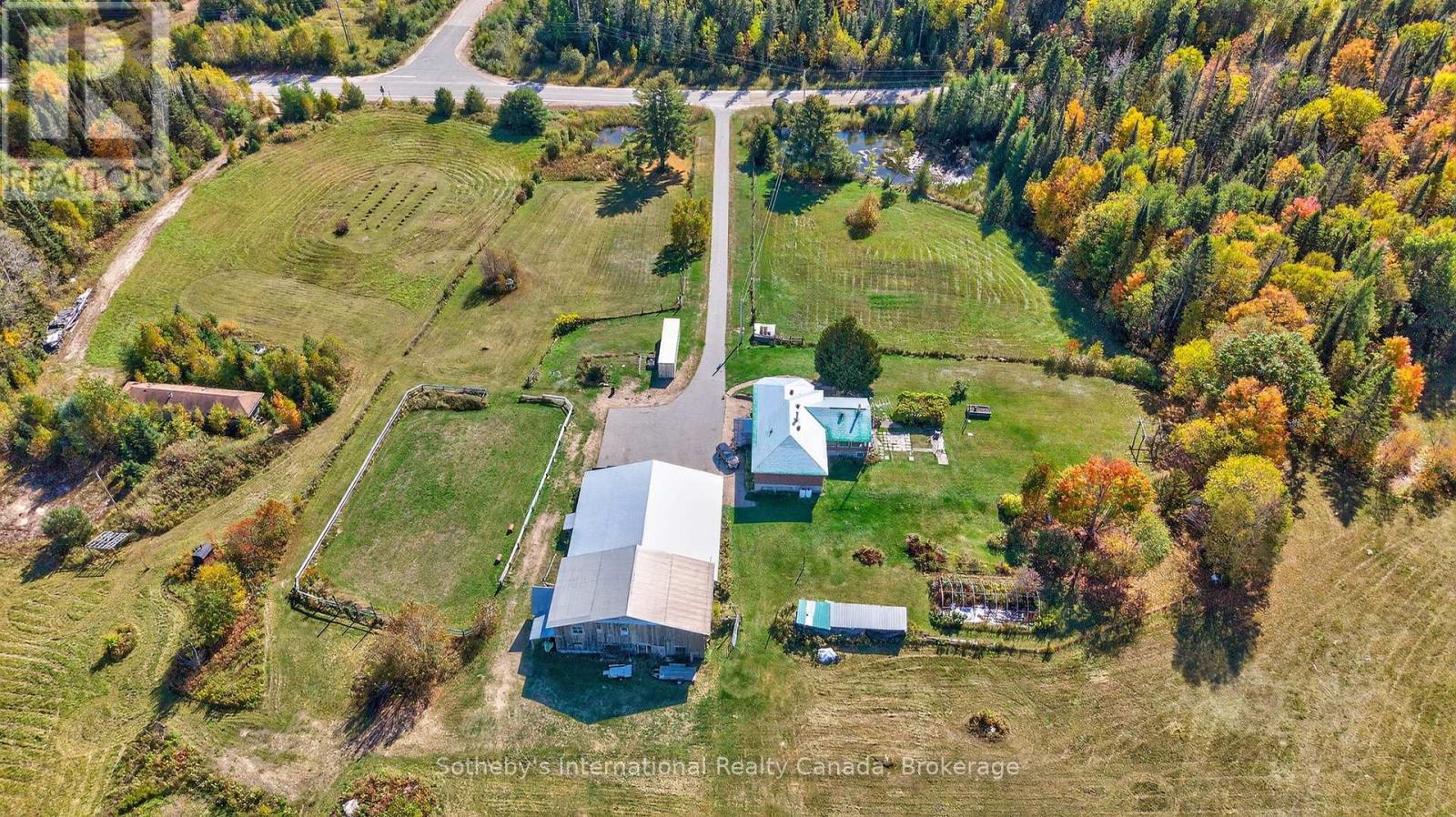 Aerial view of a rural property with a house, outbuildings, fenced paddock, and autumn woodland.