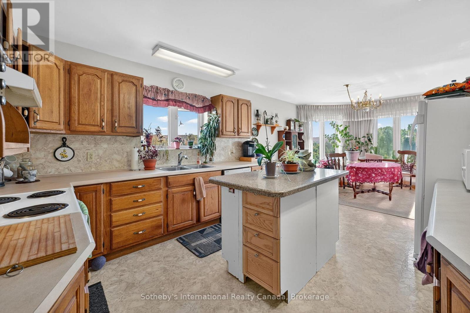 Kitchen with wood cabinets and central island, opening to a windowed dining area.