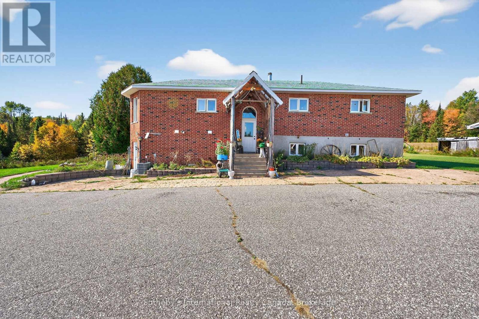 Red brick house with a timber-covered front entry, garden beds, and a wide paved driveway.