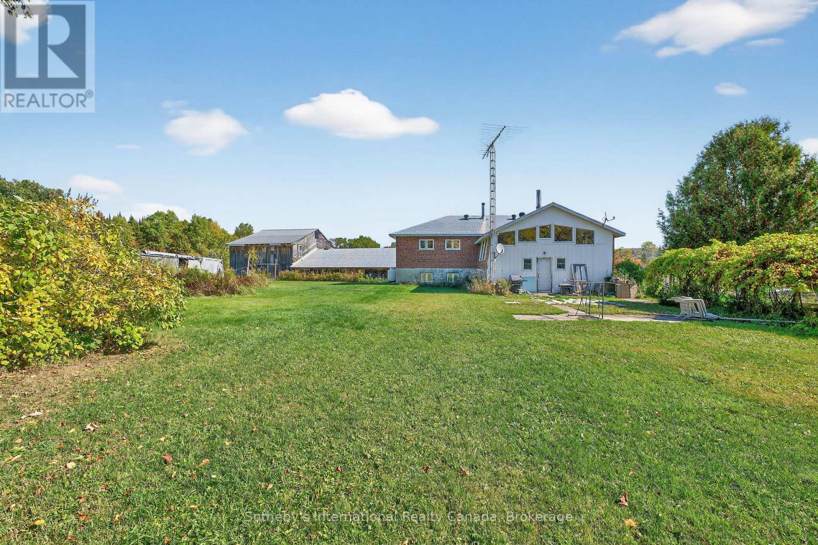 Rural house and farm outbuildings beyond a broad lawn, with mature trees and clear blue skies.