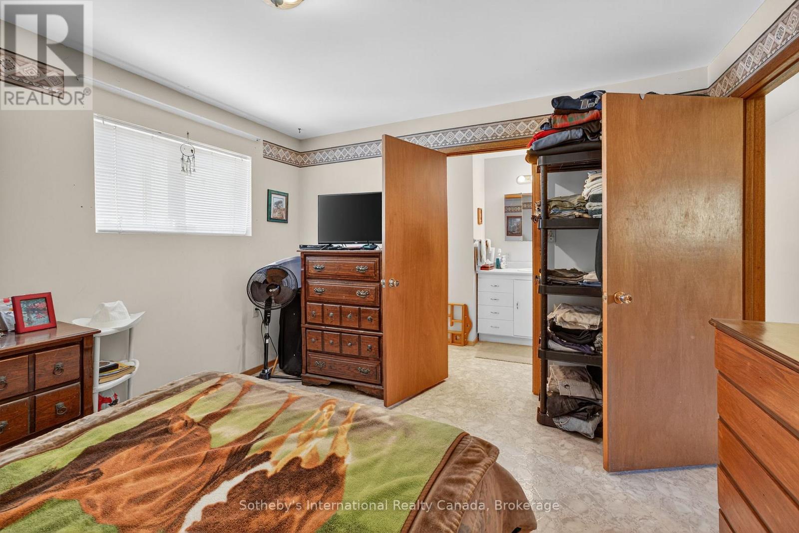 Bedroom with wooden dressers, an open clothing cupboard, and a doorway to a bathroom.